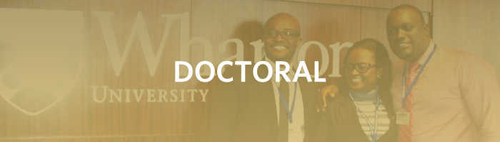A small group of people standing in front of a sign that partially reads "Wharton University" with the word "DOCTORAL" overlayed.