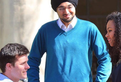 A small group of people engaged in conversation outdoors, including a person wearing a blue sweater and a turban.