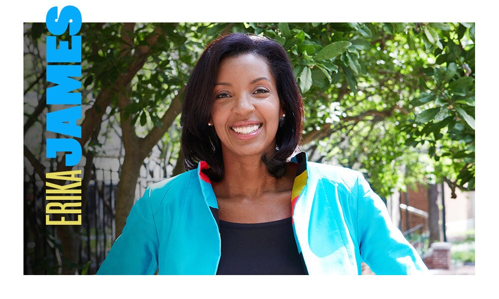 whartonDean_James-2 A person is smiling outdoors, wearing a bright blue jacket with trees in the background. The name "Erika James" is displayed vertically in bold letters.
