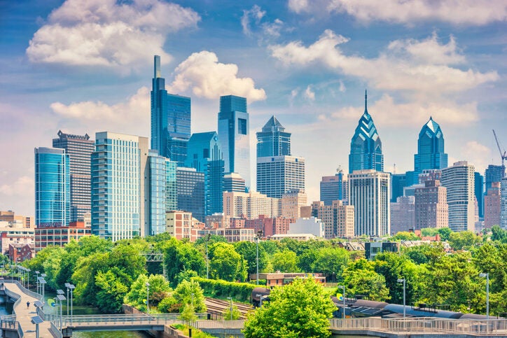 City skyline with modern skyscrapers and distinctive architectural designs, nestled above a vibrant green park, under a partly cloudy sky.