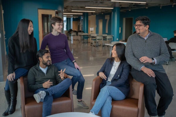 A small group of people gathered in a modern office setting, engaged in conversation and smiling, with tables and chairs in the background.