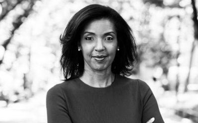 A grayscale headshot of a person with medium-length hair, wearing a top, standing outdoors with trees in the background.