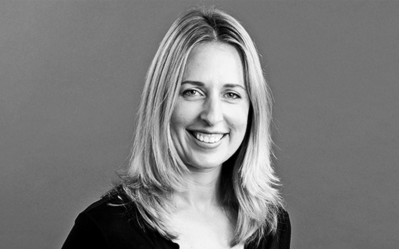 Black and white headshot of a person with shoulder-length hair, smiling, against a plain background.