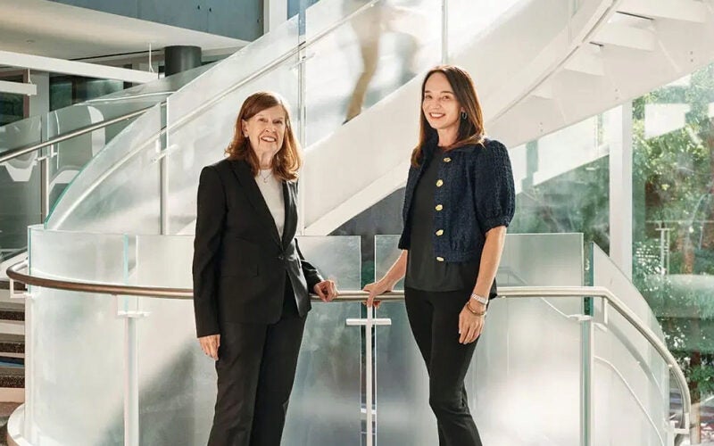 Two people standing on a modern staircase, wearing business attire, in a bright and open architectural space.