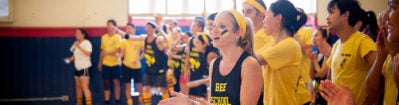 A group of people in a gymnasium, wearing matching yellow and black sports attire, appear to be cheering or participating in an event, conveying team spirit and enthusiasm.